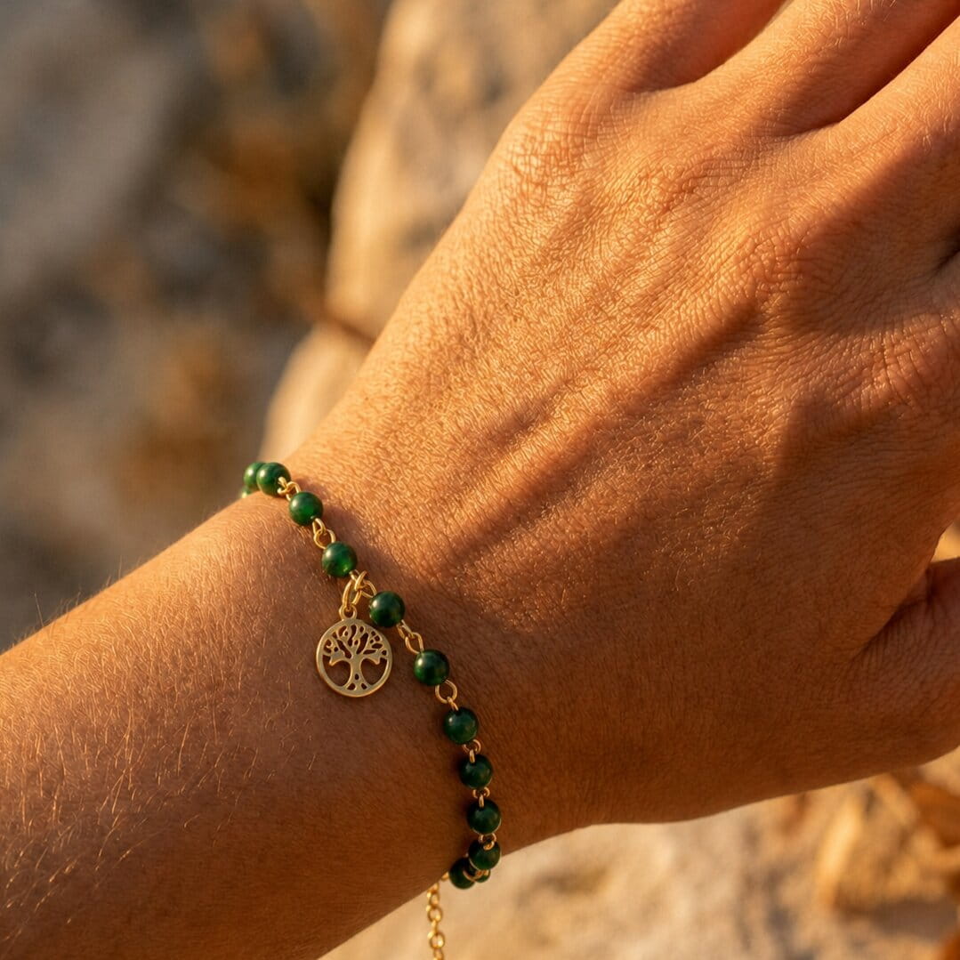 [variant: Vouves Bracelet] Hand wearing a green beaded bracelet with the Vouves tree charm against a natural background.