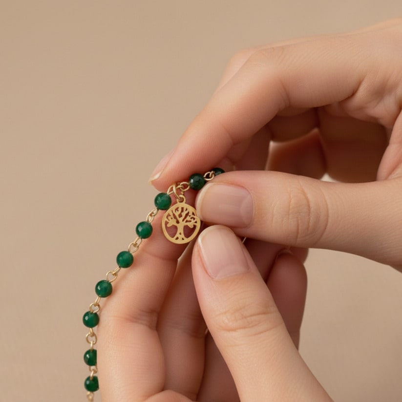 [variant: Vouves Bracelet] Close-up of hands holding a gold Vouves Olive Tree charm bracelet with green gemstone beads