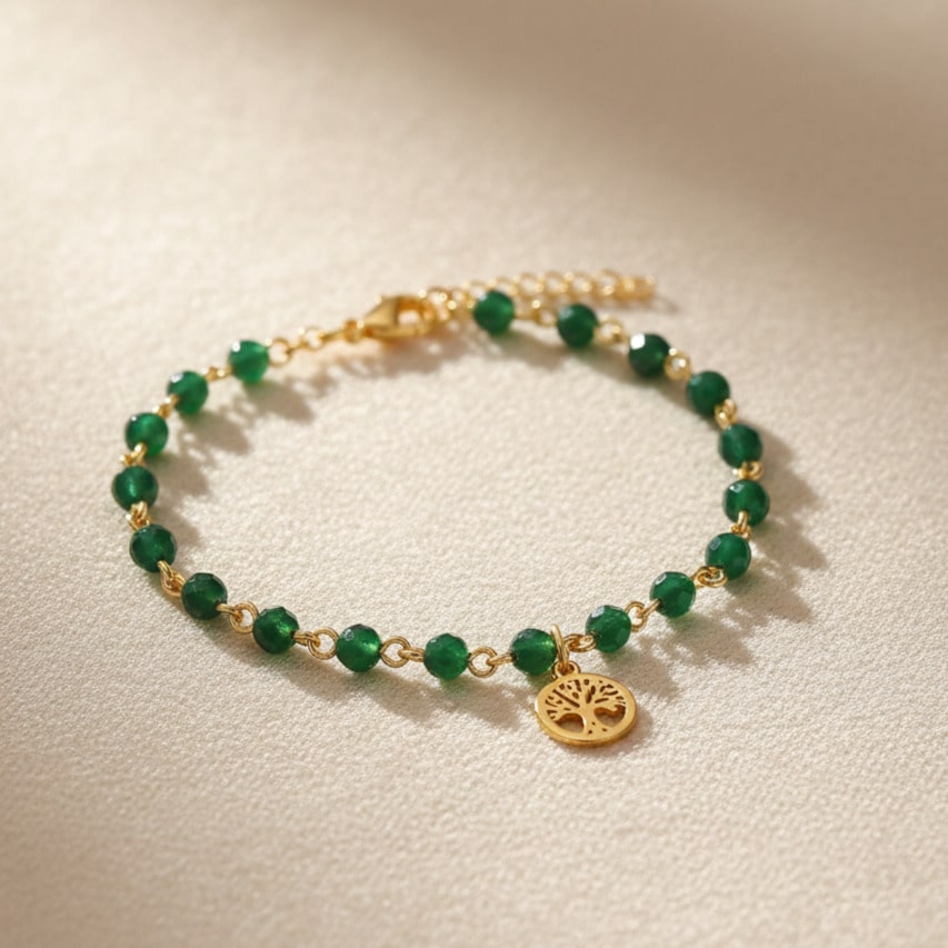 [variant: Vouves Bracelet] Gold and green gemstone bracelet featuring the Vouves Olive Tree charm displayed on a soft beige surface