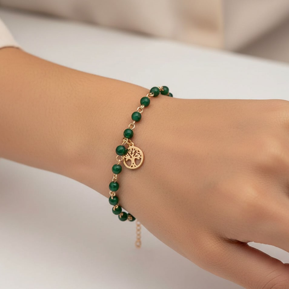 [variant: Vouves Bracelet] Vouves Olive Tree charm bracelet with faceted green beads worn on wrist against a neutral background