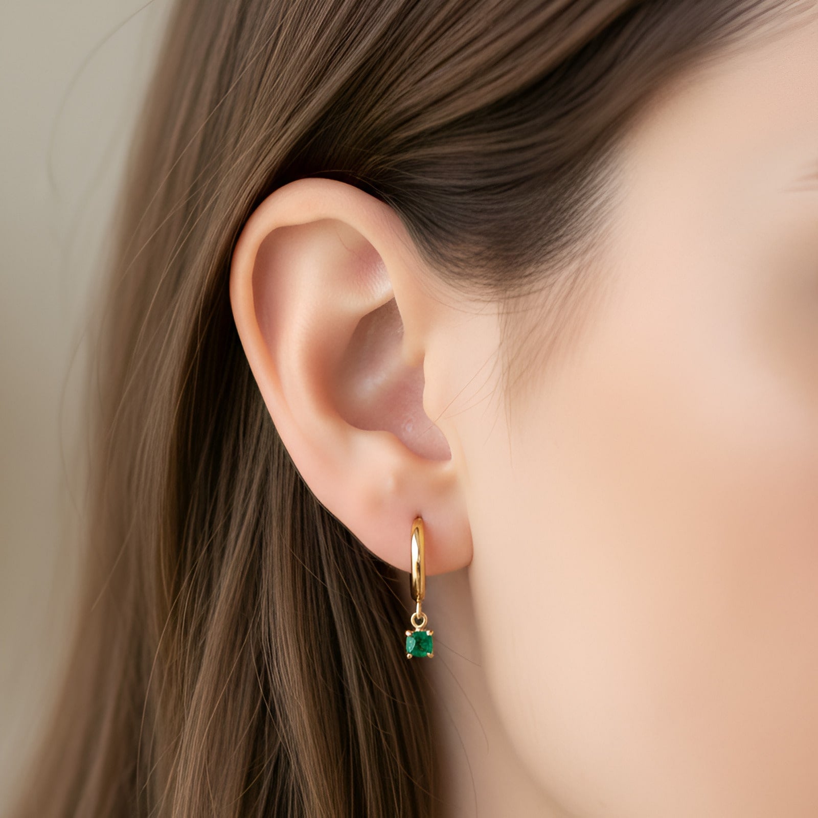 [variant:Vouves Earrings] Gold hoop earrings featuring a small green chalcedony gemstone drop worn on ear with straight brunette hair