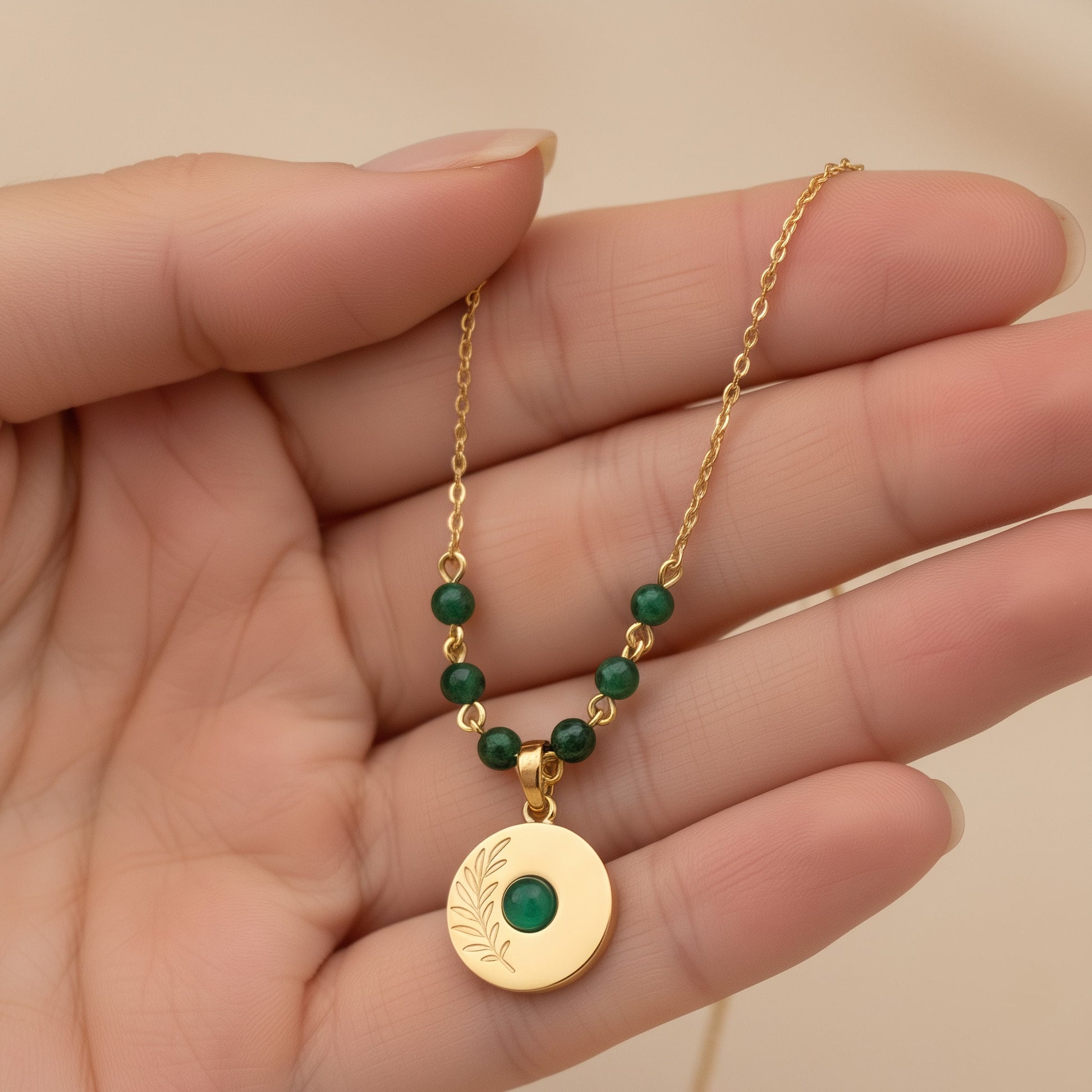 [variant:Full Vouves Collection] Gold olive branch pendant necklace with green gemstone beads held gently in hand for close-up detail