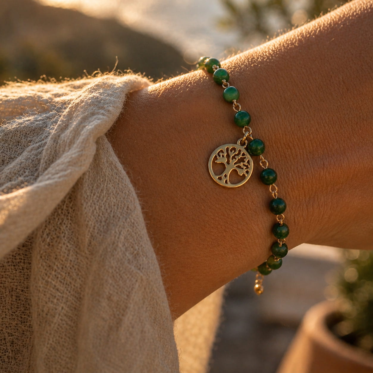 [variant:Full Vouves Collection] Green beaded bracelet with a tree charm on a wrist against a blurred natural background