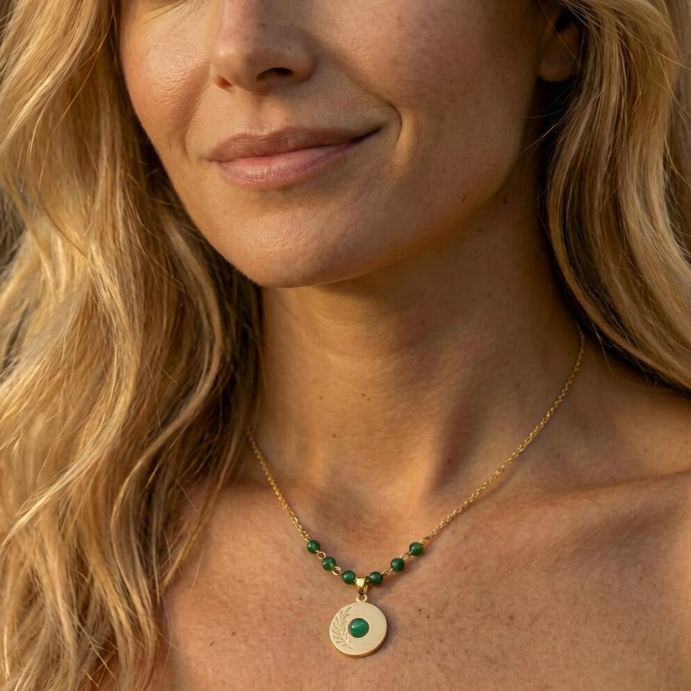 [variant: Vouves Necklace] Happy woman wearing a gold necklace with a green pendant with greek design