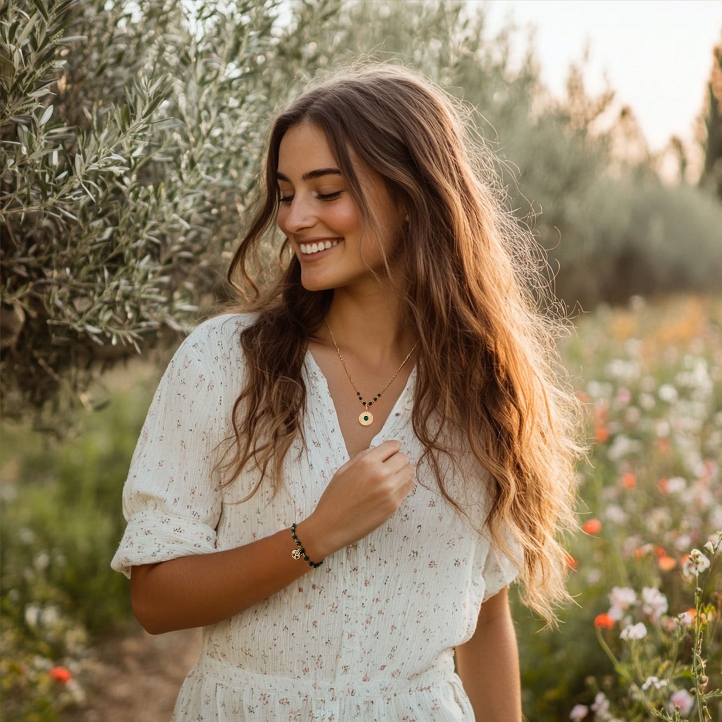 [variant: Vouves Necklace] Gold pendant necklace with green gemstone beads and matching Vouves Olive Tree bracelet worn in a Mediterranean olive grove