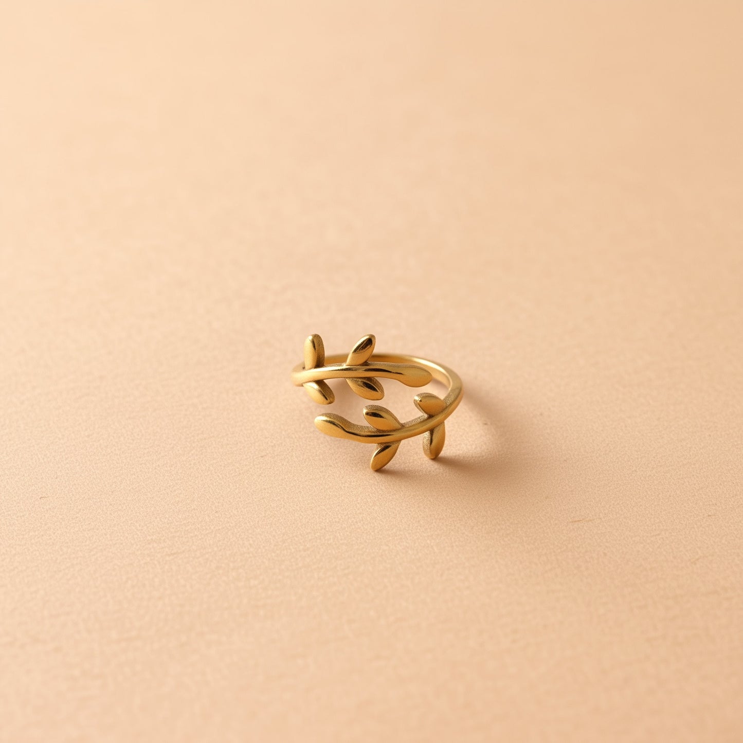 [variant:Vouves Ring] Gold olive branch wrap ring inspired by the ancient Vouves Olive Tree displayed on a soft beige background