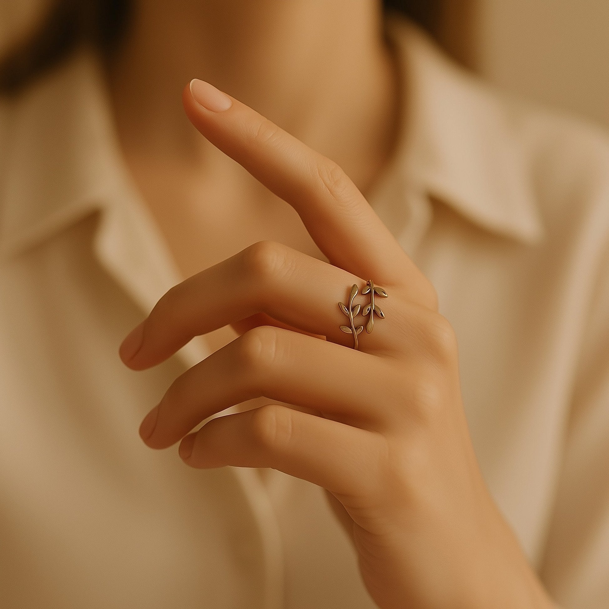 [variant:Vouves Ring] Elegant gold olive branch wrap ring worn on hand with a soft cream blouse