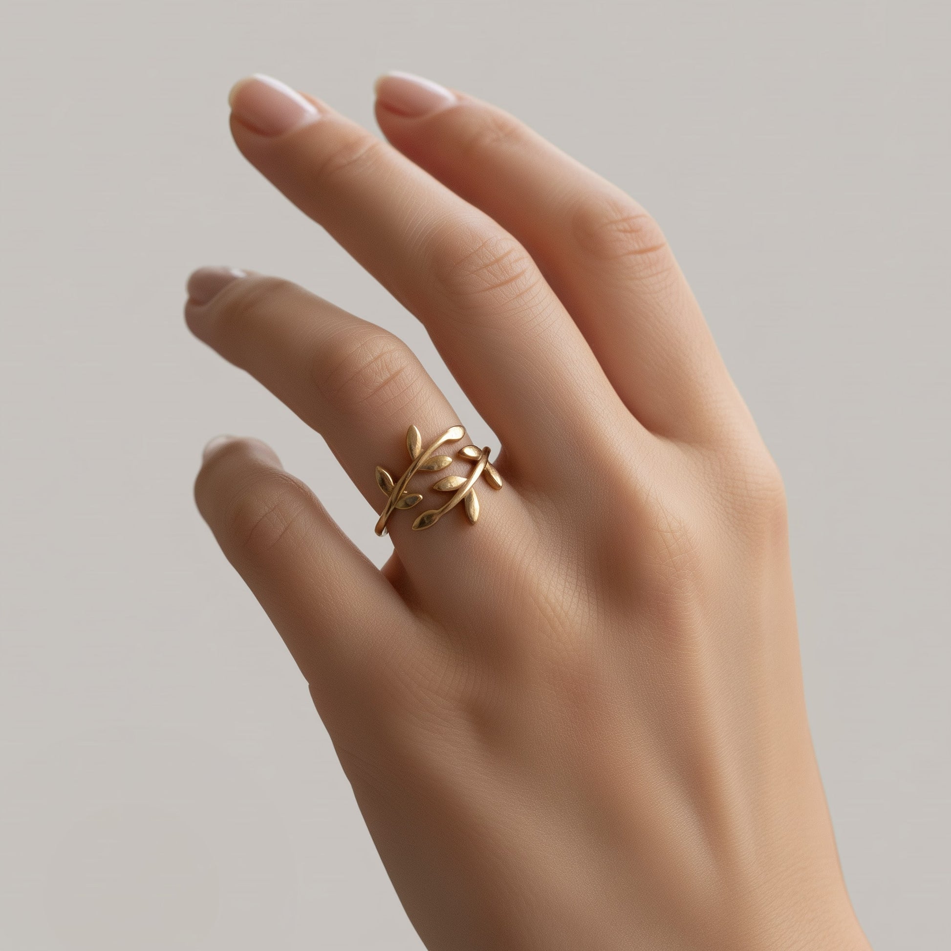 [variant:Vouves Ring] Gold olive branch ring featuring Mediterranean-inspired leaf details worn on hand against a neutral background